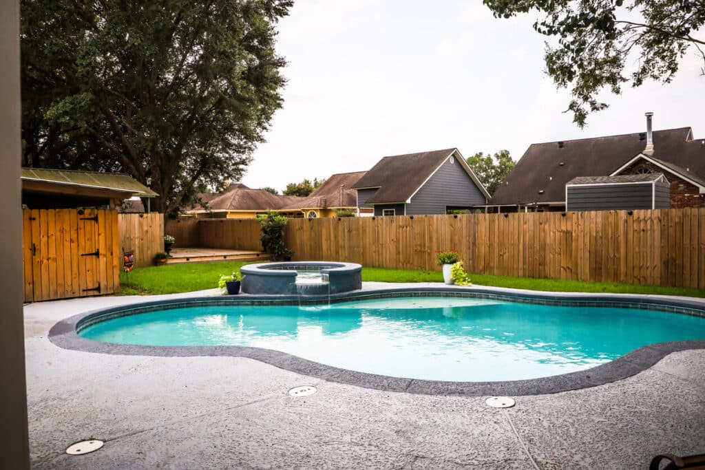 A large free form gray grey accent swimming pool with turquoise blue water in a fenced in backyard.
